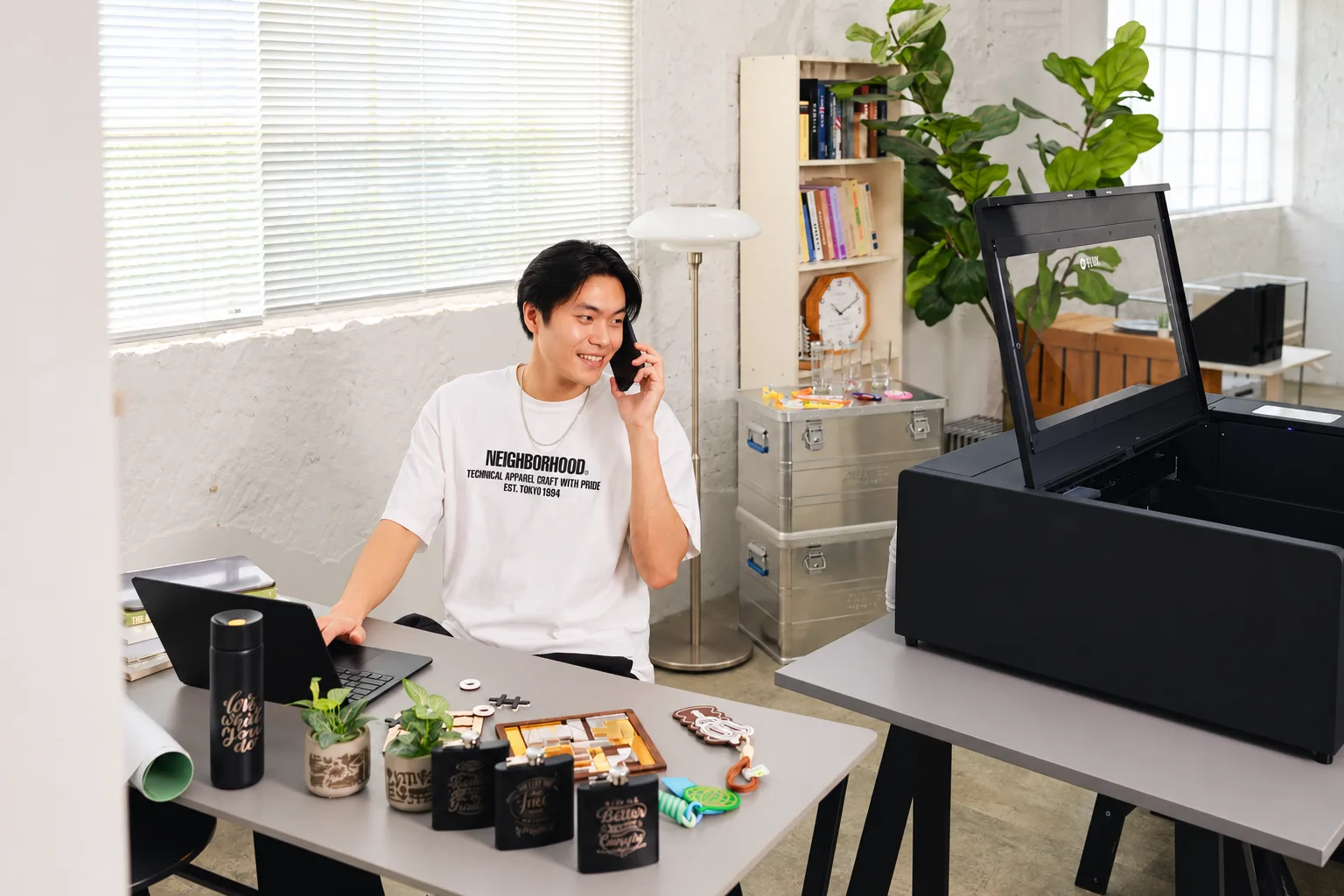 A small-business owner working beside a FLUX laser cutter and a table of finished products
