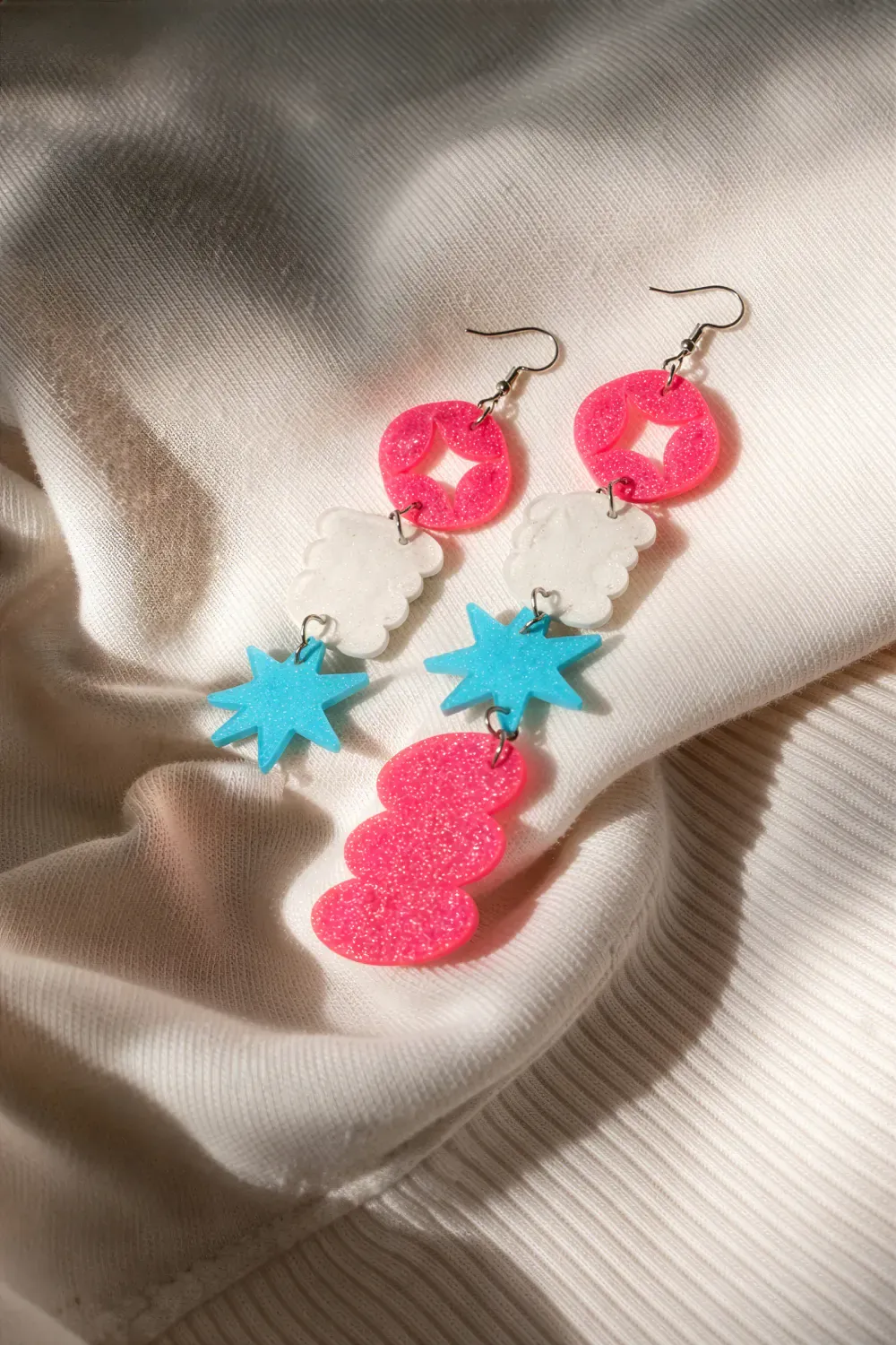 Colorful laser-cut acrylic earrings arranged on textured fabric